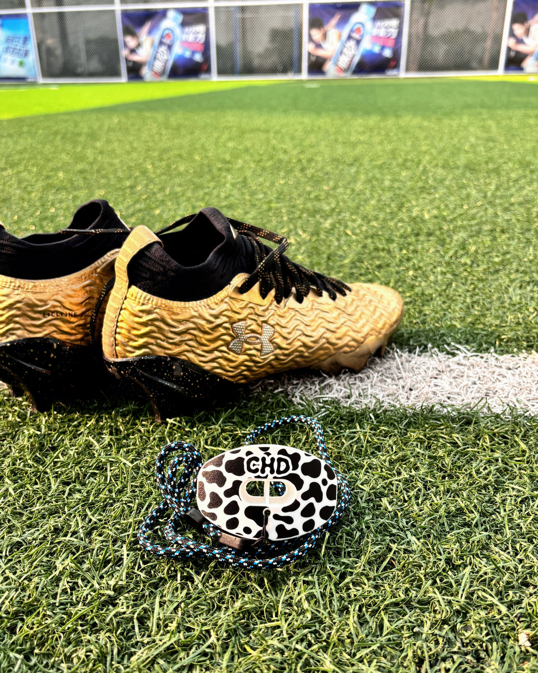 CHD Cow Print football mouthguard on turf beside football cleats