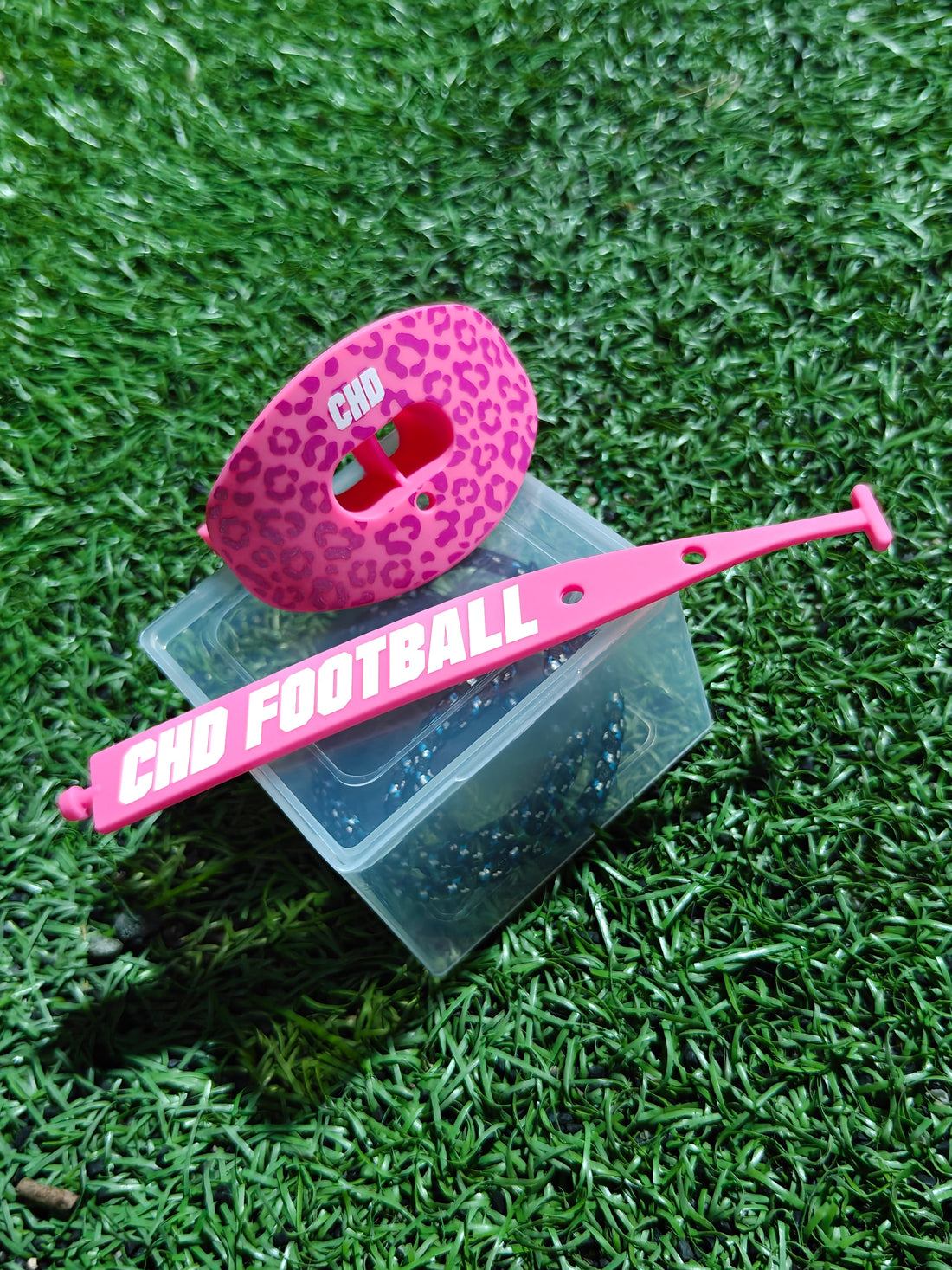Pink leopard print CHD football mouthguard and pink tether on a clear case on turf